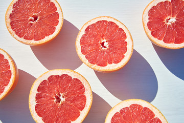 Wall Mural - Ripe grapefruit halves on white wooden background, close-up shot from above in harsh sunlight with long colored shadows.