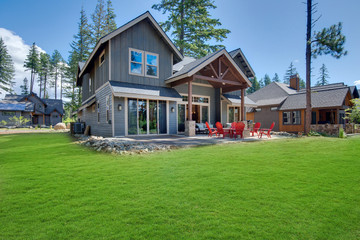 Back yard with fire pit and red chairs near newly bild luxury real estate home with forest biew and green grass.