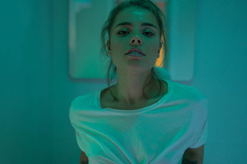 Close up portrait of beautiful sexy girl in white shirt posing in bathroom. Fashion portrait of model on a bathroom. Blue and neon lights background.