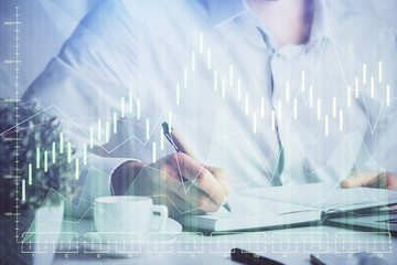 Double exposure of man's hands writing notes of stock market with forex chart.