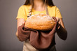 © LumenSt - Young woman in an apron with fresh bread on gray background.