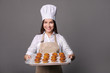 © LumenSt - Young woman in an apron with fresh bread on gray background. Cook concept