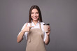 © LumenSt - Young woman in apron with coffee on  gray background. Barista concept