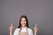 © LumenSt - Young woman in an apron on a gray background.