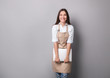 © LumenSt - Young woman in an apron on a gray background.