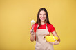 © LumenSt - Young woman in apron is standing by yellow background