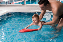 Happy Swim Coach Teaching Toddler Kid With Flutter Board In Swimming Pool