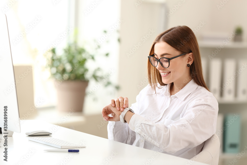 Young woman looking at her watch in office