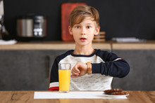 Surprised Little Boy Looking At His Watch While Having Breakfast In Kitchen