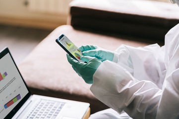 The hands of a person using the mobile phone with gloves and a safety suit against a pandemic or virus