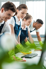 Wall Mural - selective focus of young multicultural cleaners wiping desks with rags in office