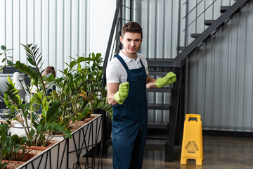 Wall Mural - handsome young cleaner in overalls and rubber gloves looking at camera