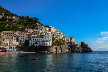 View of the beach with its bathers from the town of Amalfi from the jetty with the sea, boats and colorful houses on the slopes of the Amalfi coast in the province of Salerno, Campania, Italy.