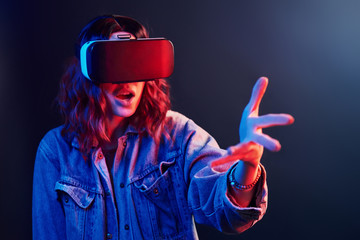 Wall Mural - Facial expression of young girl with virtual reality glasses on head in red and blue neon in studio