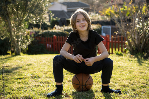 Fotografía Bambino felice seduto in giardino su un pallone da basket senza calzini