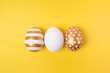 Three easter trendy colored golden decorated eggs striped pattern on yellow background. Happy Easter card with copy space for text. Minimal easter concept.