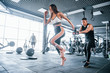 © standret - Young sportive people doing exercises together in the gym. Woman running when man holding her by elastic tape