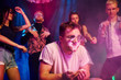 © standret - Young guy in sunglasses sniffing drug in night club with friends behind him