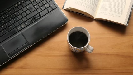 Wooden table with a laptop, a book and a cup of coffee