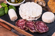 © Anna Dufour - Typical european aperitif platter with goat cheese, dry smoked sausage, pickles and bread on wooden background. France 2020.