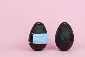 Two Isolated avocados, one wearing a surgical face mask next to another avocado that it's not wearing any 