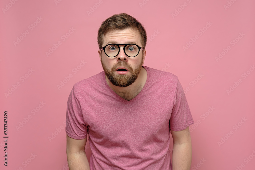 Man with glasses is confused, he leaned forward, looks with a shocked expression on his face and does not believe what he saw. - obrazy, fototapety, plakaty 