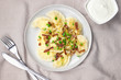 Homemade dumplings with toasted onions and bacon. Traditionally, the Ukrainian dish is decorated with green onions. Plate with dumplings on the table and sour cream. Top view
