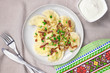 Homemade dumplings with toasted onions and bacon. Traditionally, the Ukrainian dish is decorated with green onions and a Ukrainian towel. Plate with dumplings on the table and sour cream. Top view