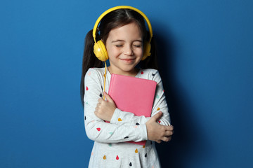 Poster - Cute little girl with headphones listening to audiobook on blue background