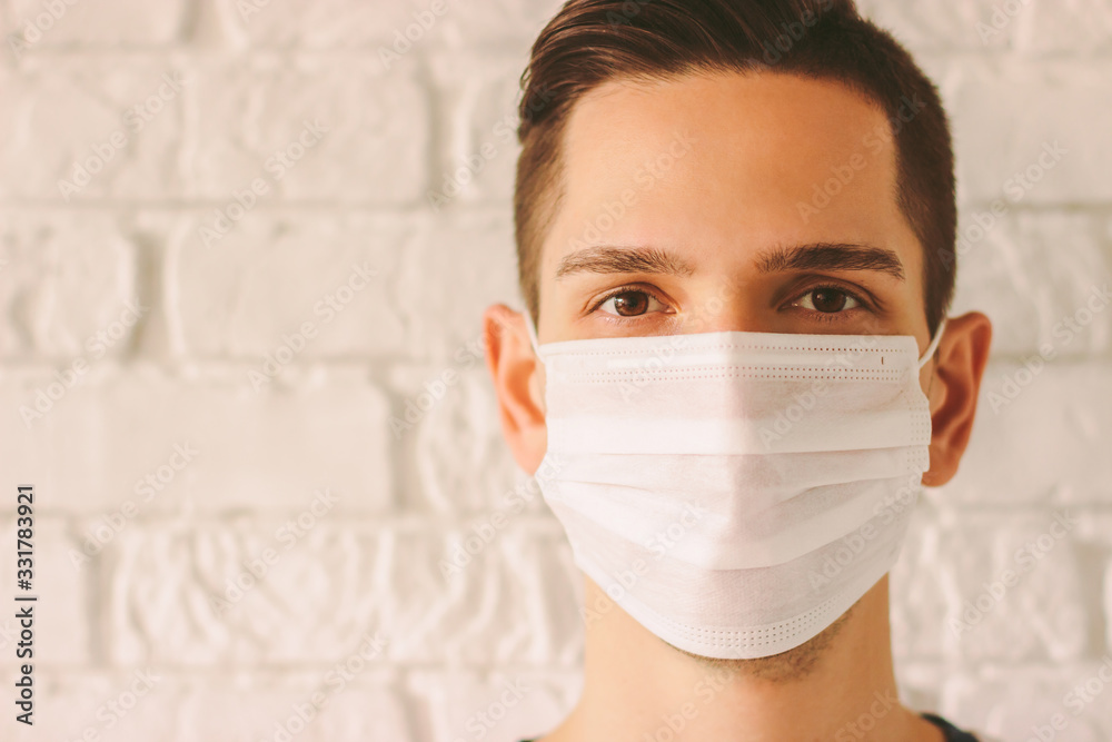 Young professional doctor in protective medical face mask against white wall. Confident medic surgeon wearing white face mask for protection against coronavirus. Preventive measures for COVID-19. - obrazy, fototapety, plakaty 