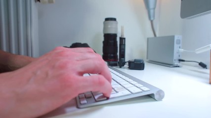 Poster - A photographer is typing a letter text on a computer keyboard while sitting at a desk. The concept of information transfer.
