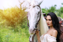 Charming Young Sexy Woman Slim Body In White Dress Standing With White Horse On Nature Background. Face Of Portrait Lady Long Black Hair With White Horse While Standing At Outdoors.
