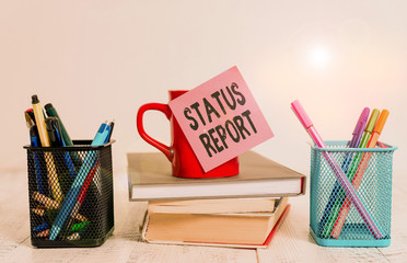Fototapete - Word writing text Status Report. Business photo showcasing document relating a situation of something such as a project Coffee cup blank sticky note stacked books pen metal holders wooden table