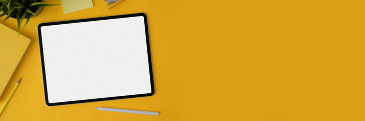 Cropped shot of blank screen tablet with stylus and stationery on yellow background
