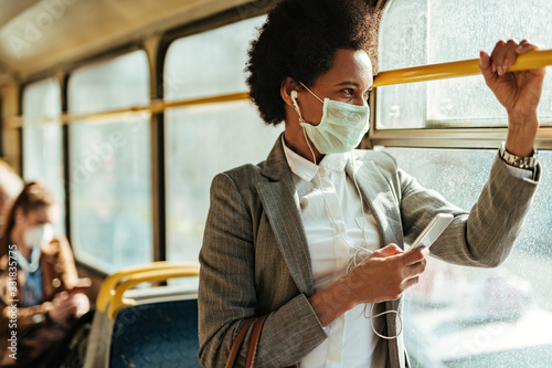 Fotografía African American businesswoman with face mask texting on the phone while traveling by bus