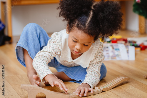 Fotomural little cute child girl enjoy playing wood puzzle on the wooden floor at home in living room