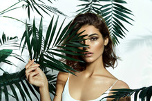 Beautiful Young Girl In The Studio On A White Background With Dark Skin, Brown Eyes And Dark Short Hair Holds A Large Green Tropical Leaf In Her Hands And Covers Part Of Her Fac
