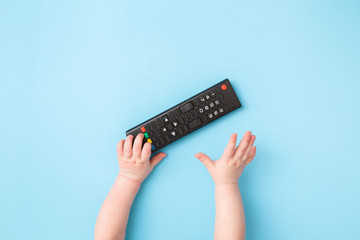 Infant hand reaching after remote control on light blue table background. Pastel color. Closeup. Favourite baby thing. Top view.