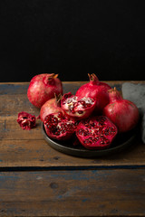 Wall Mural - Ripe pomegranates on wooden table against black wall