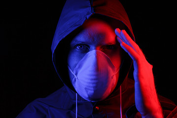 Wall Mural - A man in a protective rubber suit and a white medical mask. Virus protection. Illuminated in red and blue.