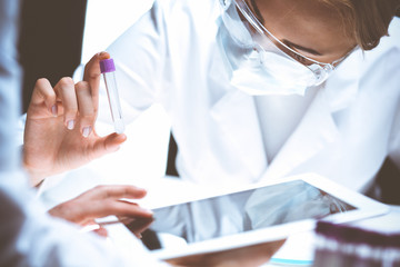 Wall Mural - Coronavirus pandemic. Professional female scientist in protective eyeglasses researching tube with reagents in laboratory. Concepts of medicine and virus protection