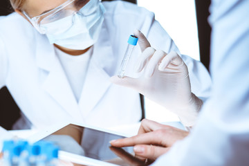 Wall Mural - Coronavirus pandemic. Professional female scientist in protective eyeglasses researching tube with reagents in laboratory. Concepts of medicine and virus protection