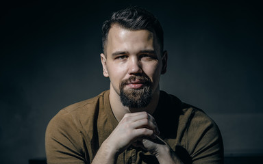 portrait of a young man with a beard in a brown t-shirt on a dark background