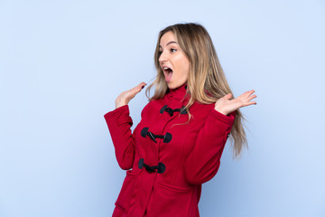 Young woman with winter coat over isolated blue background with surprise facial expression