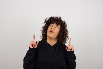 Wall Mural - Portrait of beautiful elegant woman over isolated background being amazed and surprised looking and pointing up with fingers showing something strange.