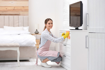 Poster - Young chambermaid wiping dust from furniture in hotel room