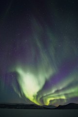 dancing green northern lights in the night sky over a mountain range in lapland finland