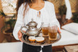 Woman hands holding silver tray with traditional moroccan mint tea, cookies and vintage teapot. Hospitality and service in Morocco.