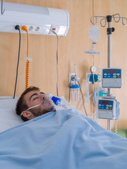 teenage boy with a beard and wearing an oxygen mask, in a hospital room