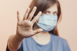 © fantom_rd - young woman in medical protective mask shows a stop gesture with hand on studio background, girl held out palm with fear, concept of quarantine measures